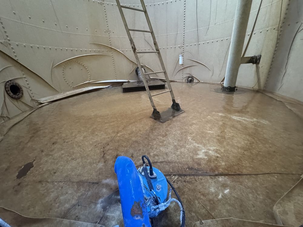 Inside a drained steel water tank, with a blue pump on the sediment-covered floor and a ladder to the hatch.