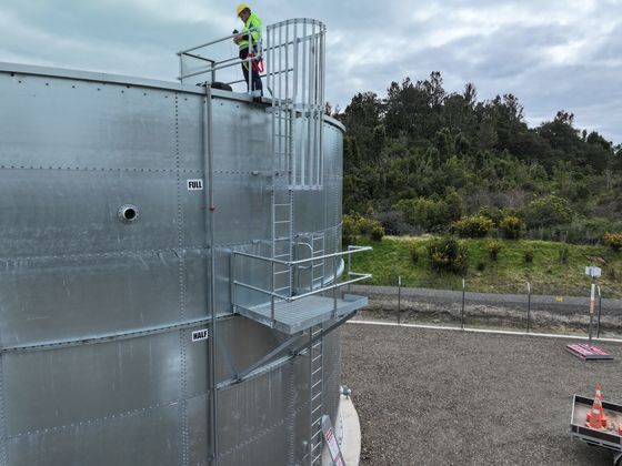 A galvanised steel fire water tank with an access ladder and a worker in hi-vis on the top platform.
