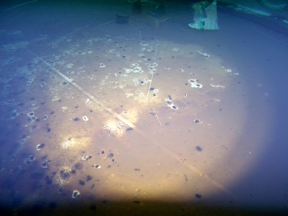 Settled sediment and debris across the floor of a steel water tank, lit by the ROV.