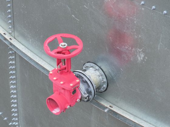 A pink gate valve on the outlet of a galvanised steel tank.
