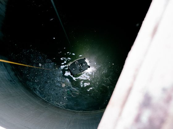 Looking down through a tank hatch at a remotely operated crawler with its lights on, working in dark water below.