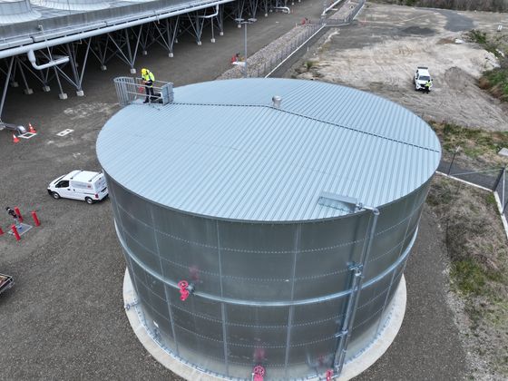 Drone view of the roof of a galvanised steel tank, with a worker at the open access hatch.