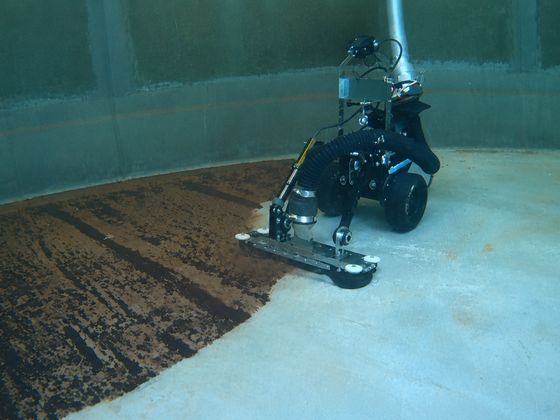 The VAC Boss crawler on a reservoir floor, with a clean strip of concrete beside the brown sediment it is removing.