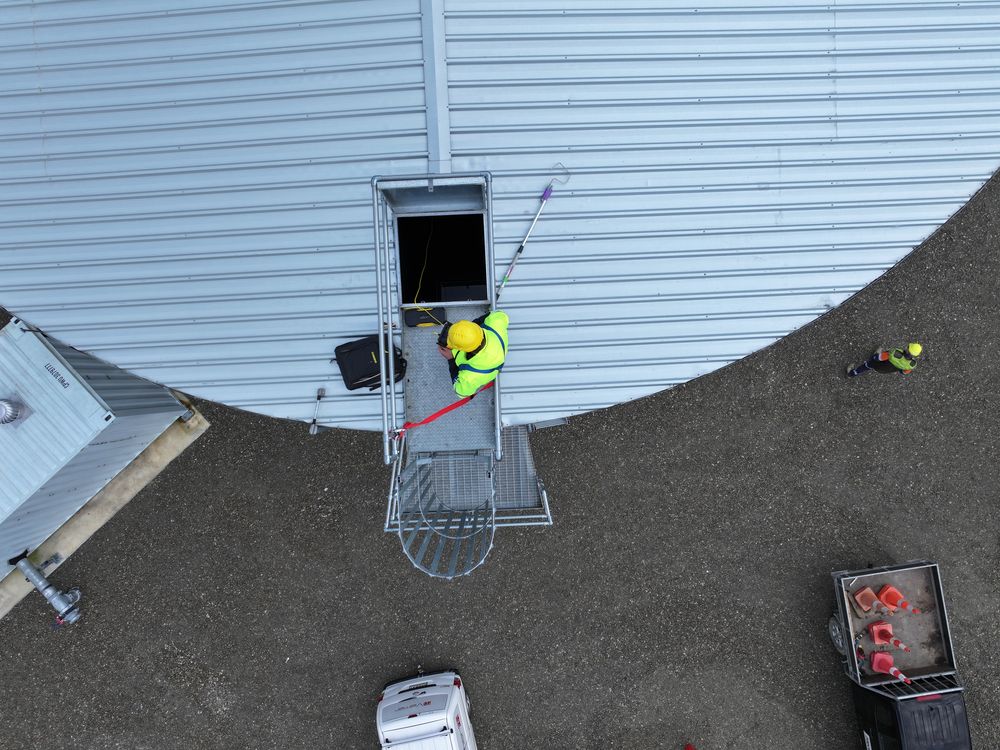 Aerial view straight down onto a round tank roof, with a worker in hi-vis at the open hatch.