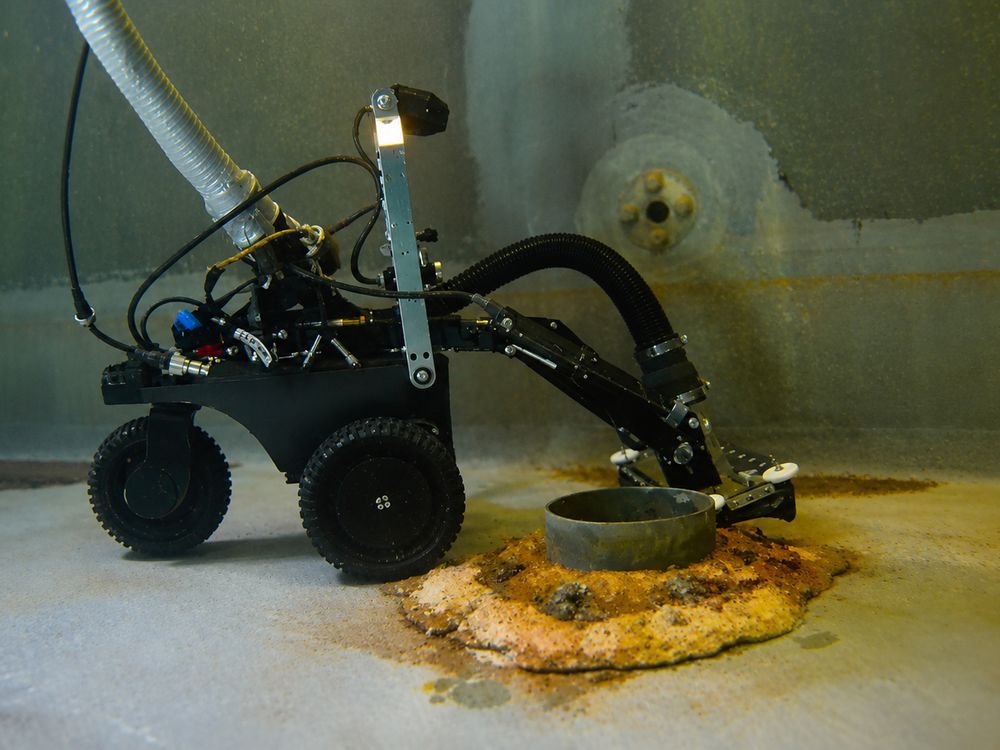 The VAC Boss crawler working beside a corroded floor flange, its suction hose running up out of frame.