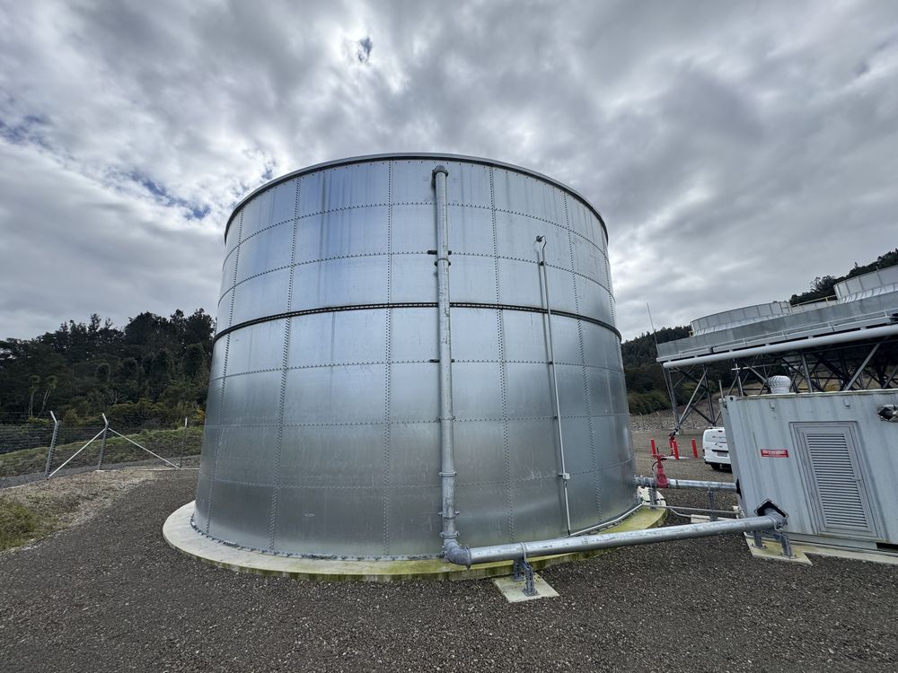 A galvanised steel water tank and its pipework under a dramatic cloudy sky.
