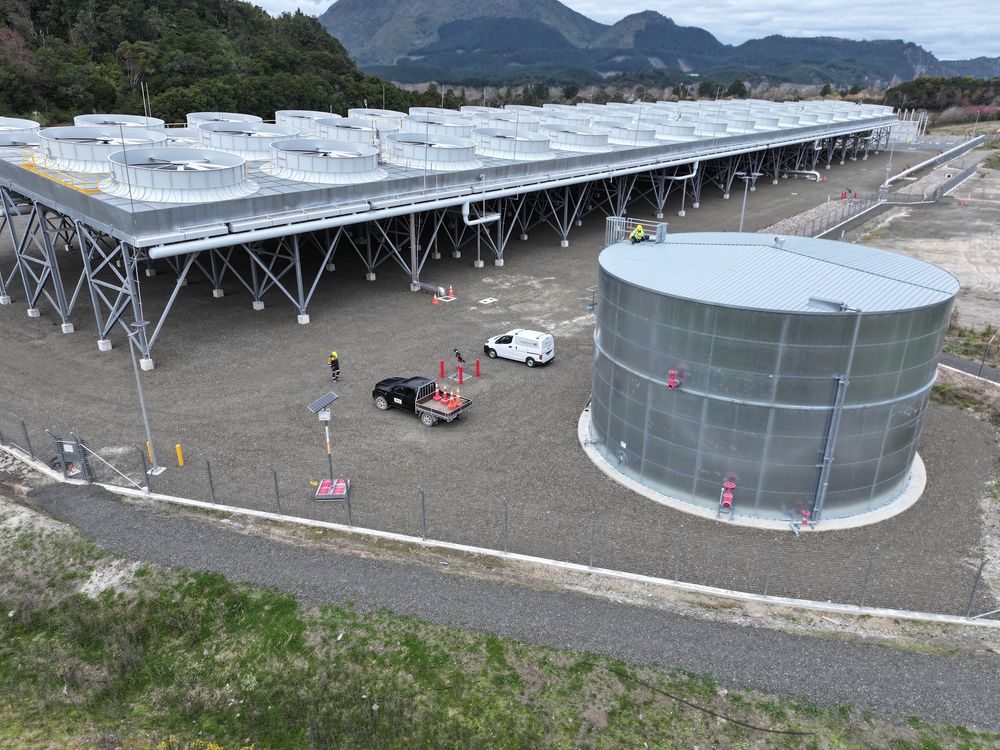 Aerial view of a galvanised steel water tank in front of a large industrial cooling structure.